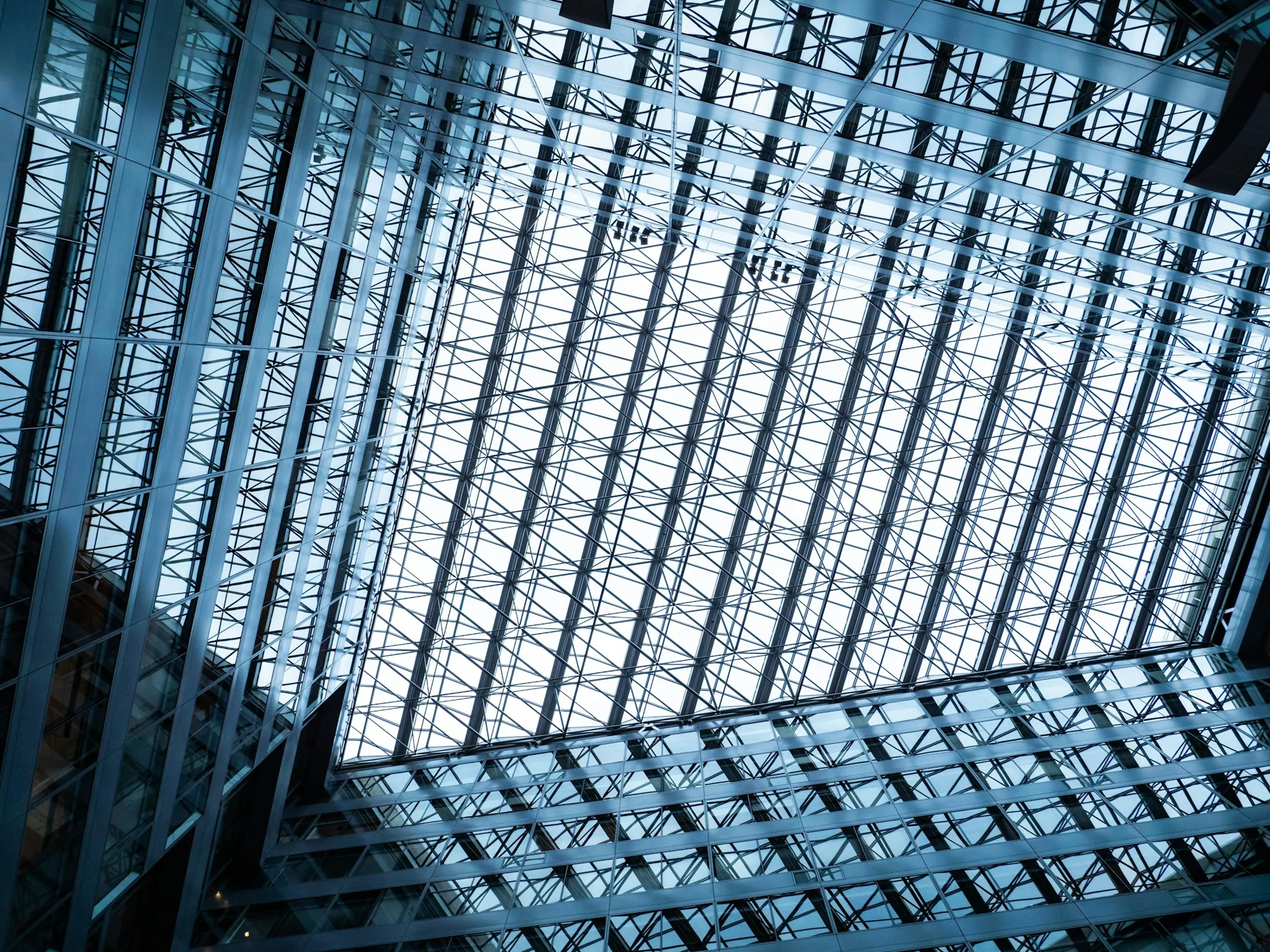 Blue steel beams and reflected glass framing the geometric roof of a modern atrium